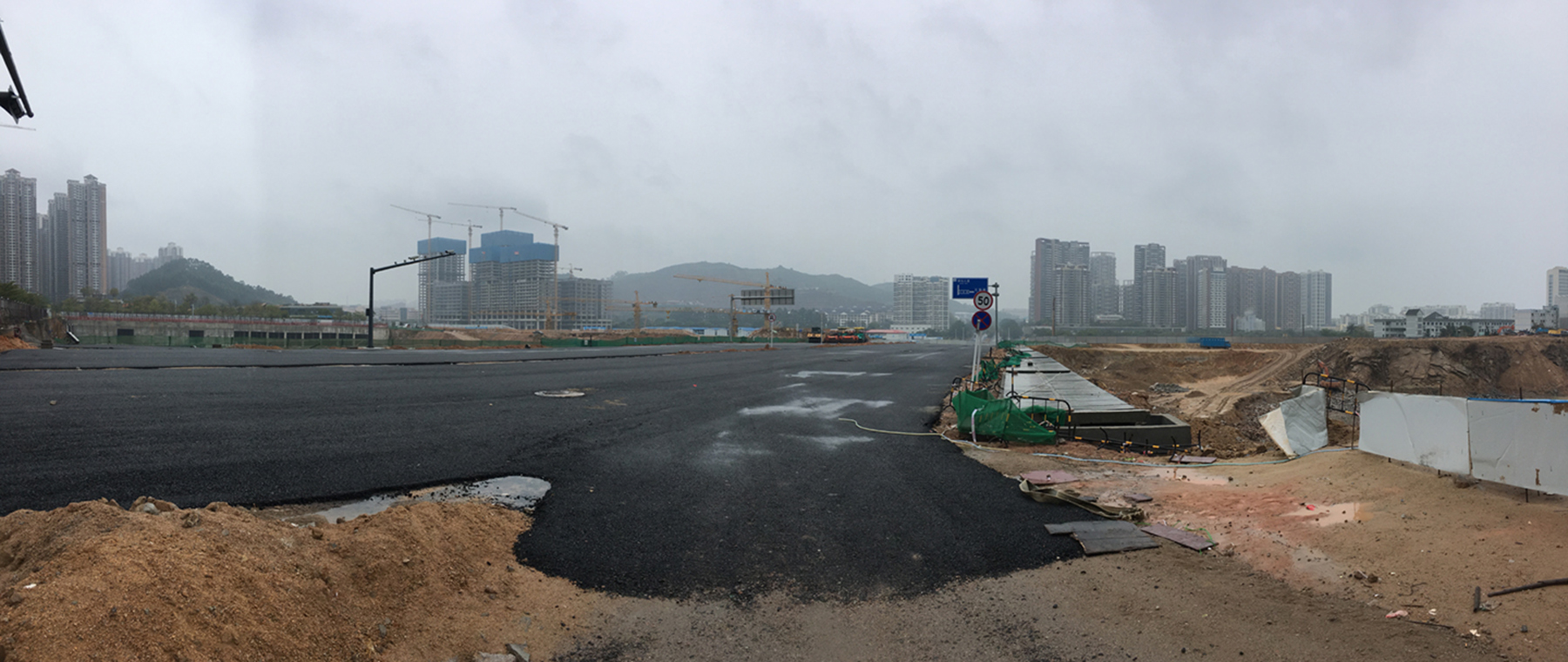 A broad, partly paved construction site at Shenzhen’s Vanke Design and Innovation Center, with exposed earth, cranes, distant towers, and hazy hills beyond.