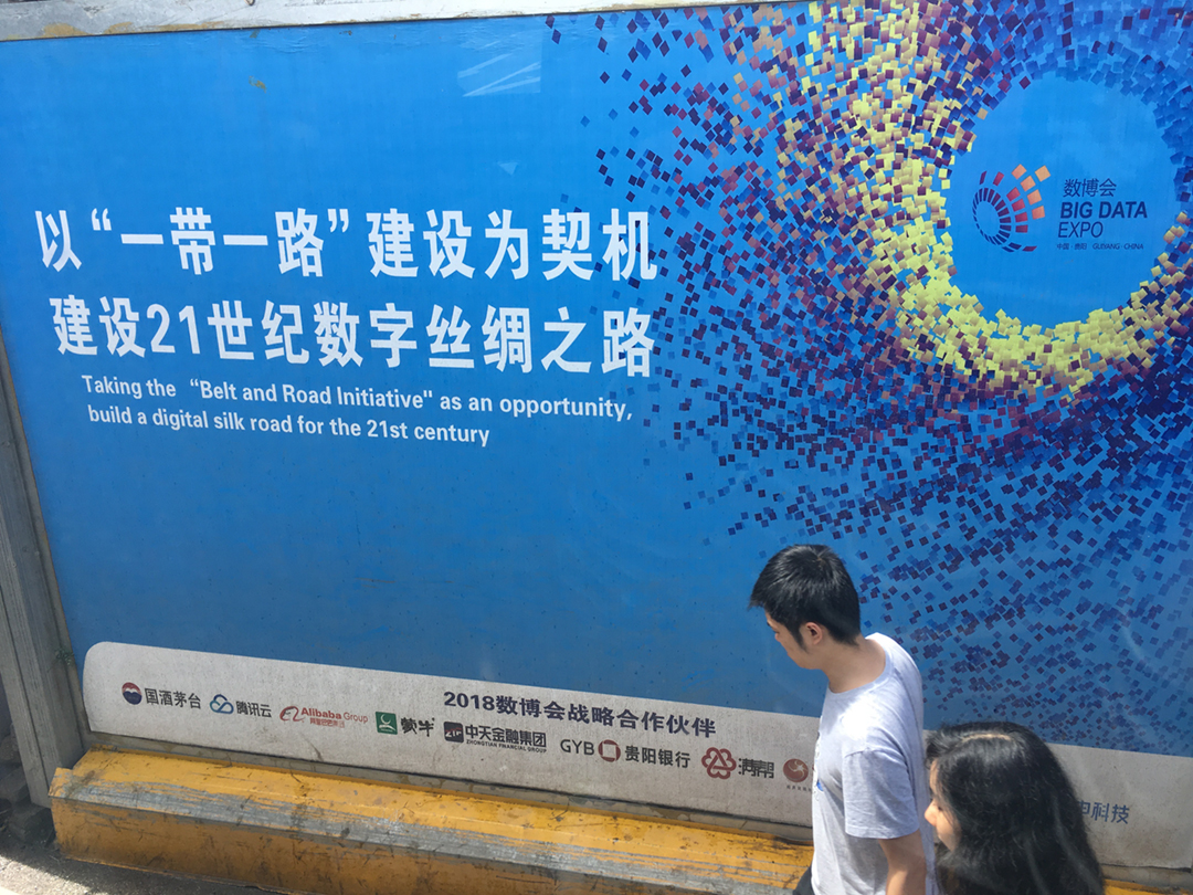Pedestrians pass a blue billboard in Guian New Area. Chinese and English text calls for taking the Belt and Road Initiative as an opportunity to ‘build a digital silk road for the 21st century.’