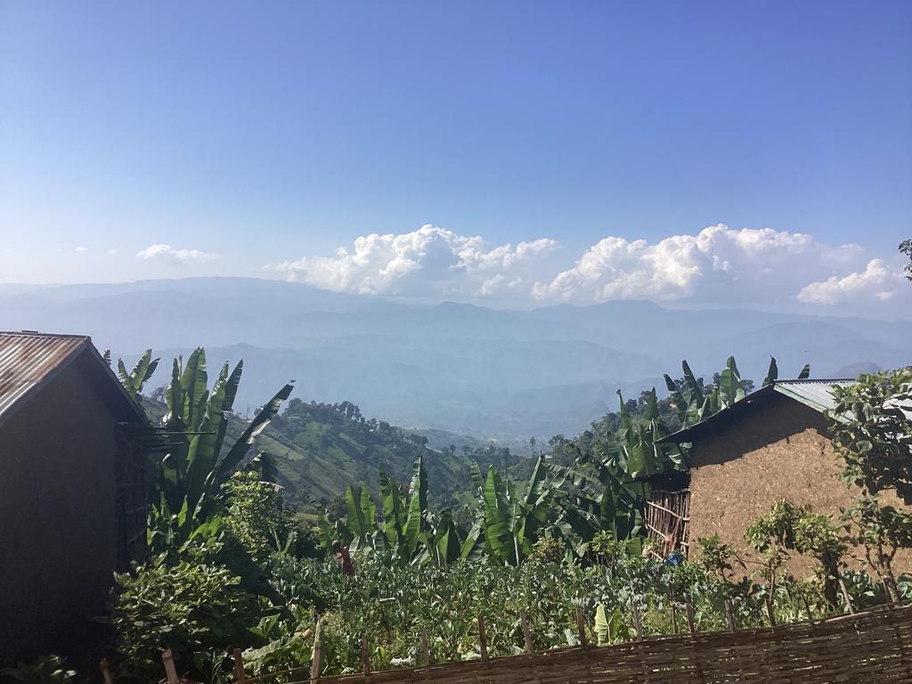 Earthen houses in Ethiopia against backdrop of sky and mountains.