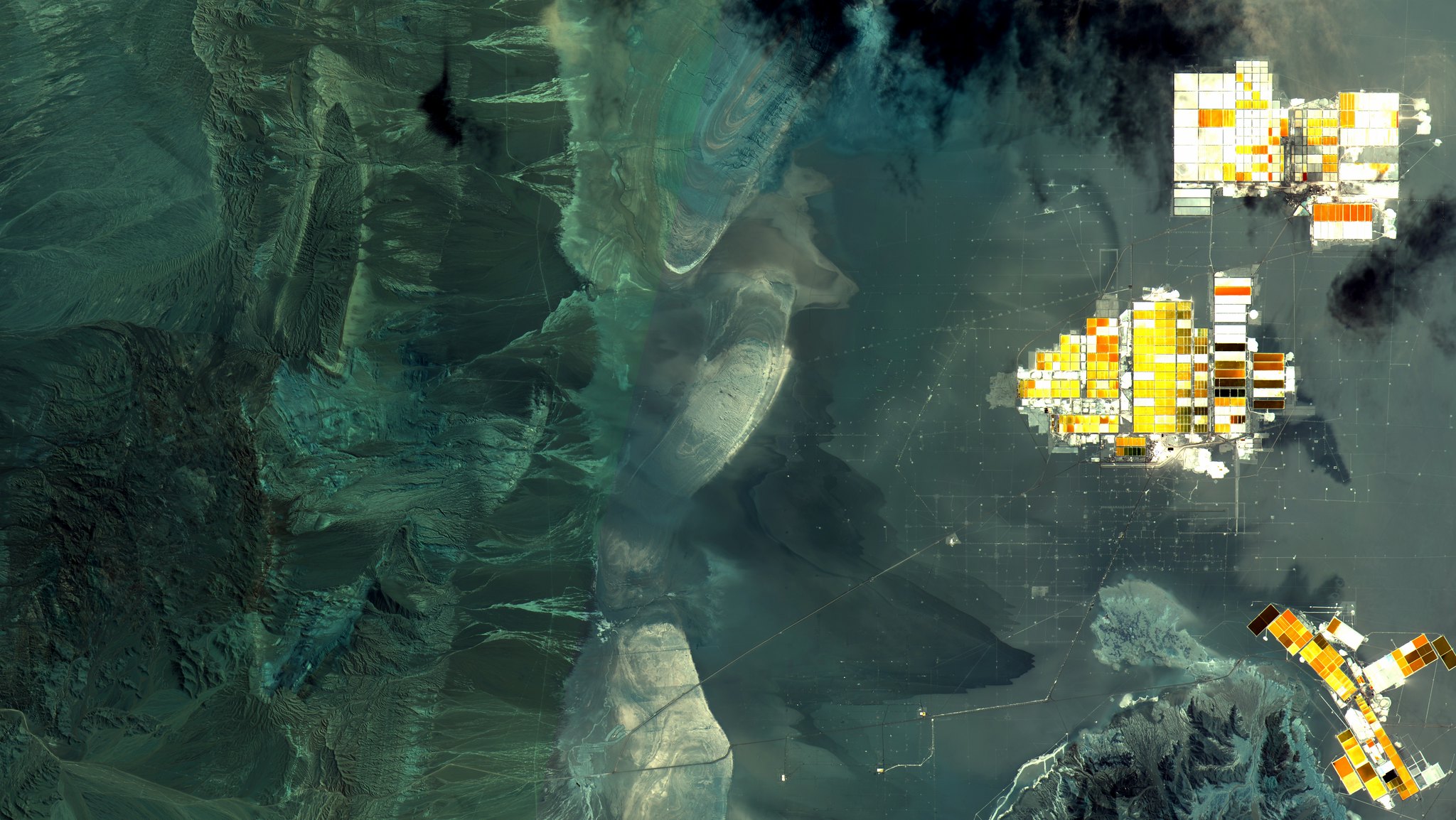 A satellite image showing dark mountainous terrain on the left and bright quadrilateral shapes on the right.
